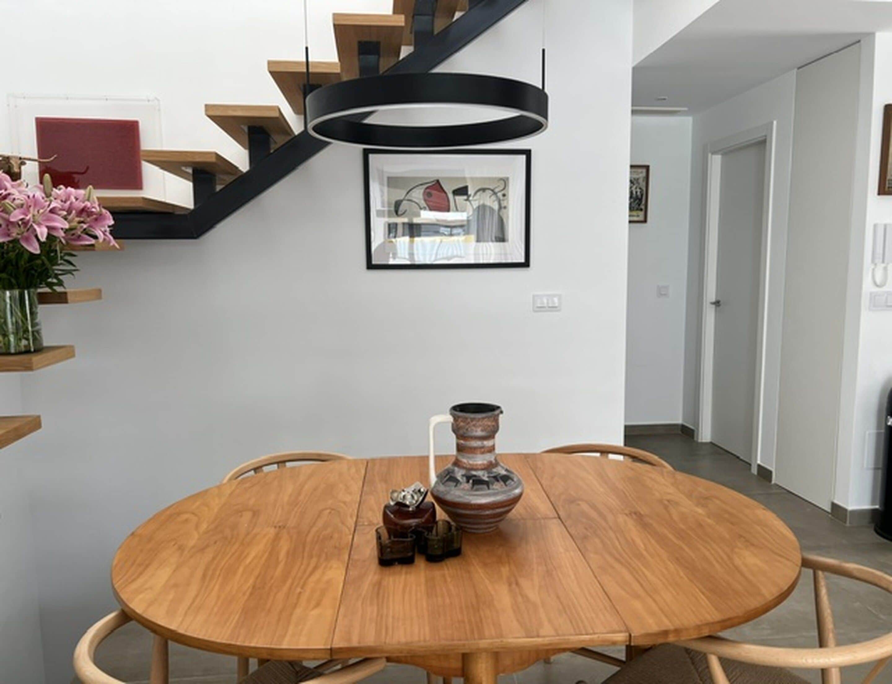 A dining area with a round wooden table, chairs, a vase, and a framed picture on the wall.