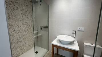 A modern bathroom with a glass shower enclosure, a pedestal sink, and a toilet.