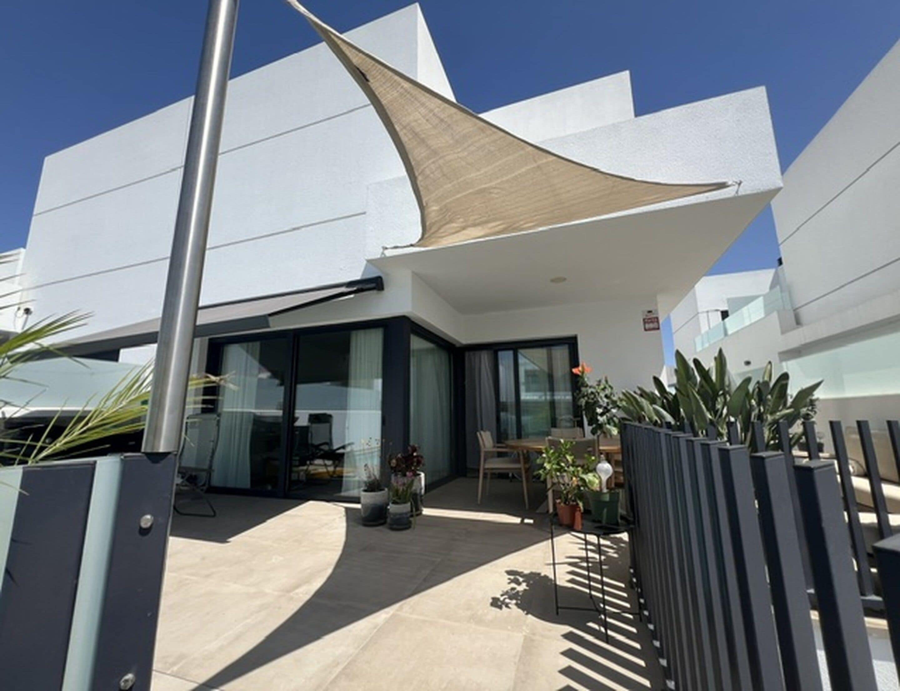 A modern building with a large glass entrance, outdoor seating area, and a distinctive sail-like shade structure.