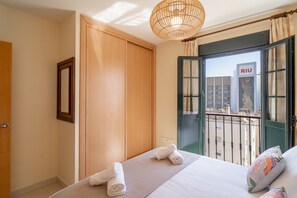 A hotel room with a bed, a wooden wardrobe, a balcony with a view of a building labeled 'RIV', and a hanging light fixture. - Apartment in Nerja Near Beaches & Pool (Nerja)
