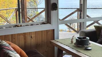 A cozy room with a wooden bench, a table with a cup and a book, and a window overlooking a body of water and mountains.