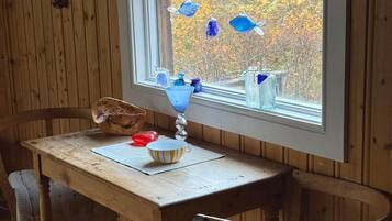 Una mesa de madera con un cuenco y una lámpara, dos sillas y una ventana decorada con adornos de peces de vidrio azul.