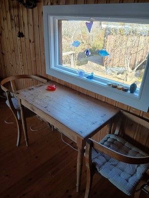A wooden table with a window view of a garden, a chair, and a vase with candles.