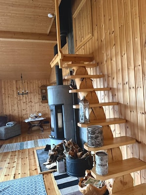 A wooden interior with a fireplace, shelves, and a staircase.