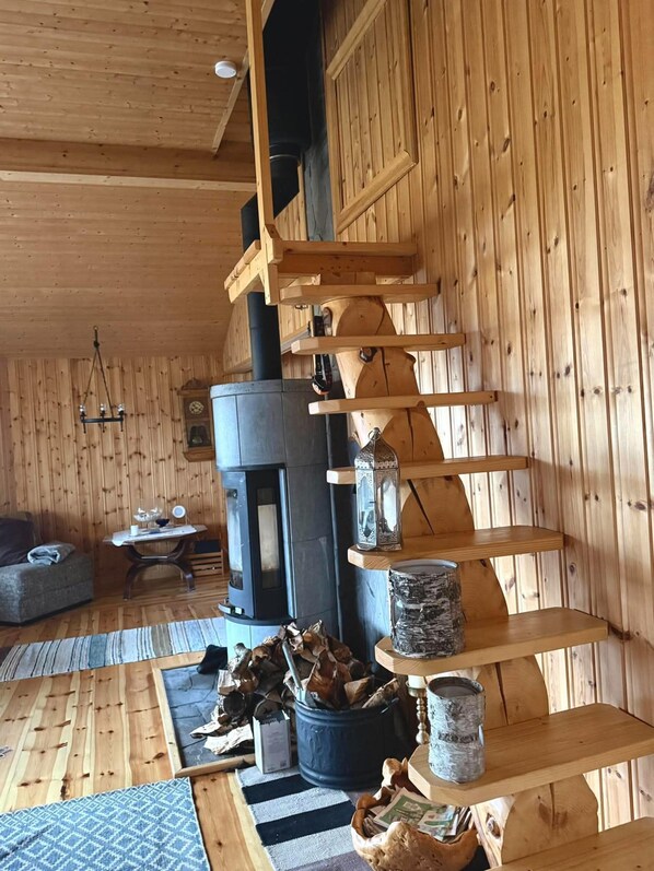 A wooden interior with a fireplace, shelves, and a staircase.