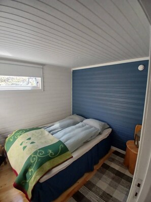 A small, single-bed room with a window, a blue wall, and a wooden floor. - Off grid cabin by the sea in Eidsfjorden (Hadsel)