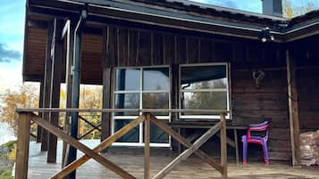Une cabane en bois dotée d’une terrasse, de grandes fenêtres et d’une cheminée.
