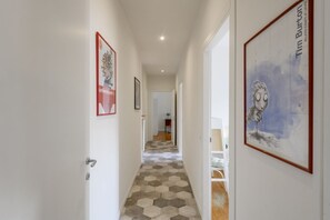 Un passadís amb paviment de disseny hexagonal, parets blanques i quadres emmarcades.