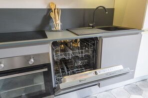 Eine kleine Küche mit Spülmaschine, Backofen und integriertem Spülbecken.