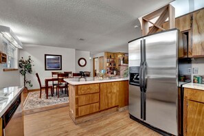 A modern kitchen with a stainless steel refrigerator, wooden cabinets, a marble countertop, and a dining area with chairs and a table. - Secluded Glamping Site in Eustis, Florida, with Hot Tub, Fire-Pit and Forest Views (Eustis)