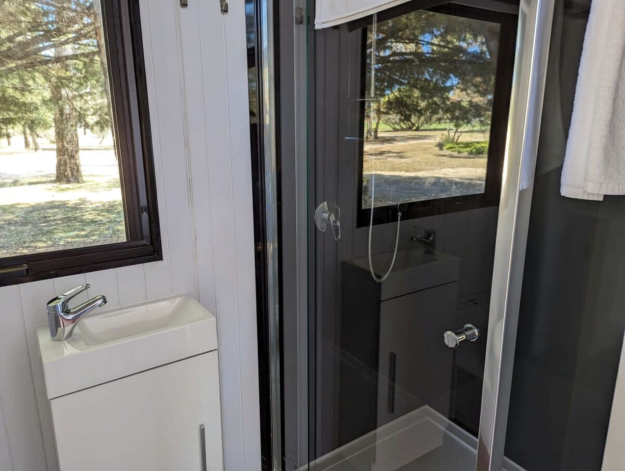 A bathroom with a white sink, a glass shower enclosure, and a view of an outdoor area.