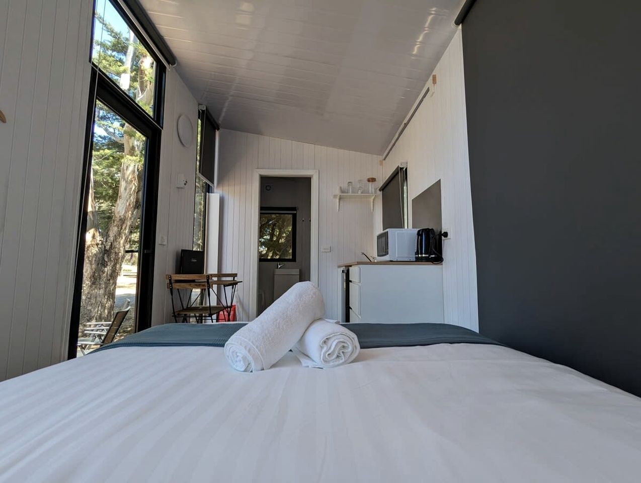 Habitación de hotel con una cama grande, un escritorio, una silla, un televisor y una ventana con vistas a árboles.