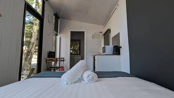 Habitación de hotel con una cama grande, un escritorio, una silla, un televisor y una ventana con vistas a árboles.
