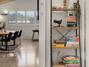 A room with a dining area, a bookshelf with various board games, and a telescope on a shelf.