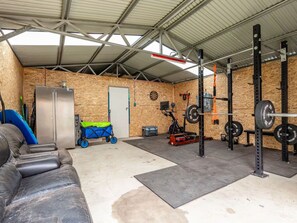 Et fitnessrum med styrketræningsudstyr, et stort spejl og en blå træningshjul.