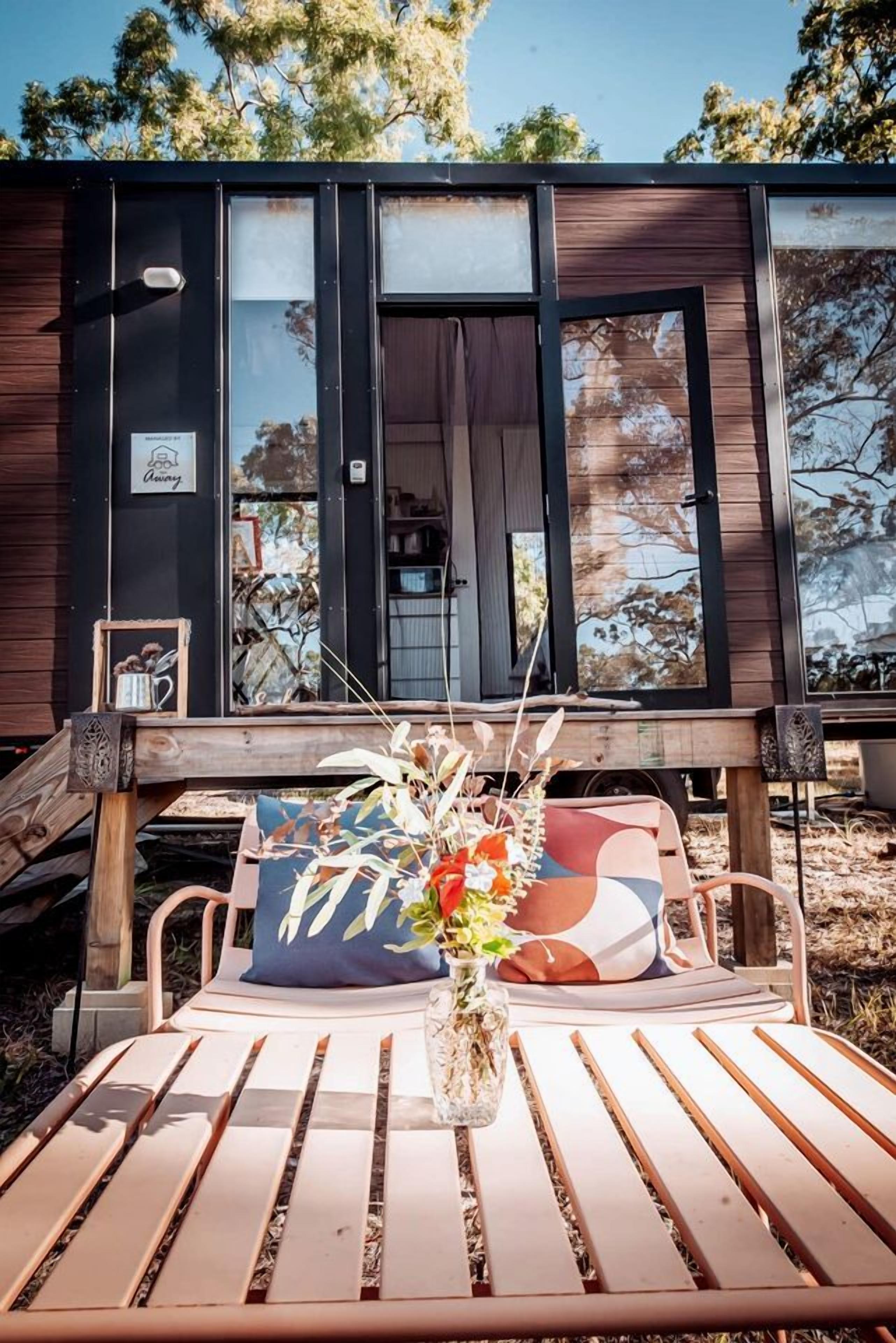 A modern cabin with a wooden deck, a dining table with a vase of flowers, and a sign indicating a 'Charming' atmosphere.