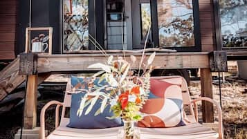 A modern cabin with a wooden deck, a dining table with a vase of flowers, and a sign indicating a 'Charming' atmosphere.