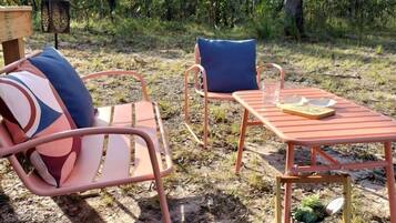 Un espacio al aire libre con dos sillas de metal y una mesa, rodeado de árboles.