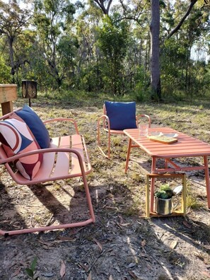 Un espacio al aire libre con dos sillas de metal y una mesa, rodeado de árboles.