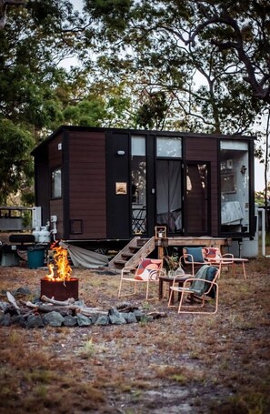 A small cabin with a fire pit, outdoor seating, and a view of trees.