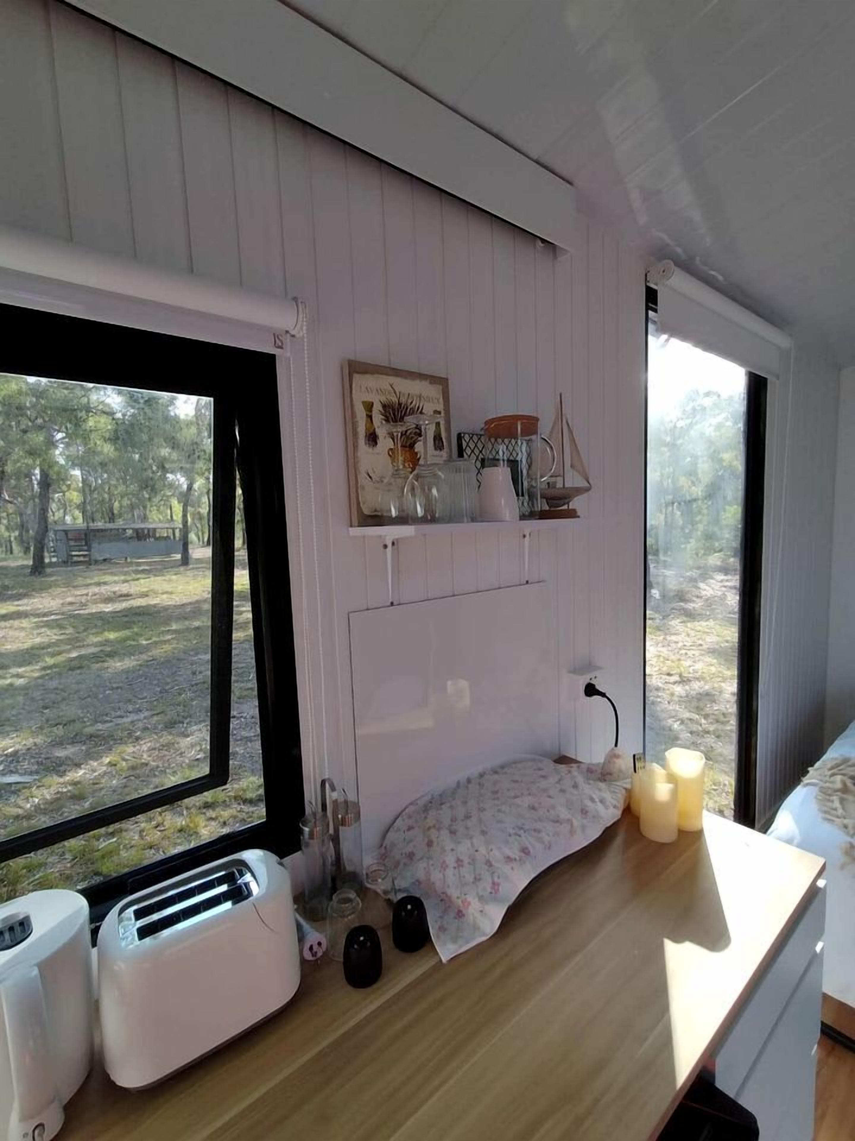 Une petite cuisine avec une fenêtre, un grille-pain, une bouilloire et une petite étagère ornée d’objets décoratifs.