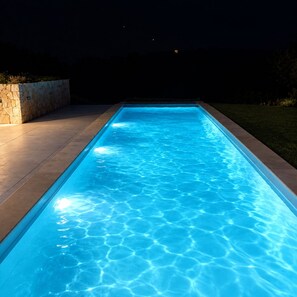 Ein rechteckiger Swimmingpool mit klarem, blauem Wasser, umgeben von einer Steinmauer und einer gepflasterten Terrasse.