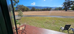 A view from a window overlooking a grassy area with a wooden deck and two chairs.