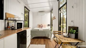 Habitación de hotel compacta con cama, mesita de noche y vistas amplias a través de grandes ventanales.