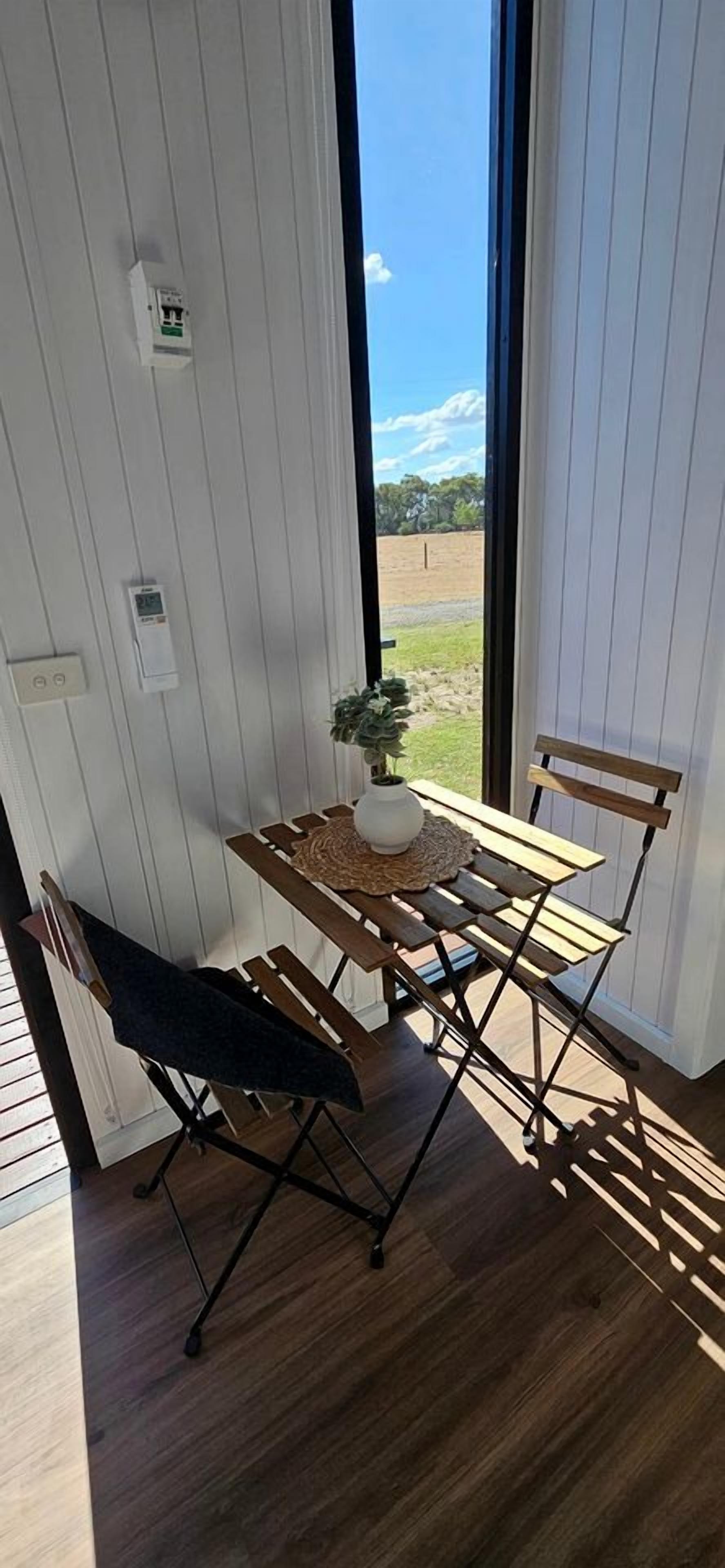 Una habitación con una mesa y sillas de madera, una planta en maceta y vistas a través de un ventanal amplio.