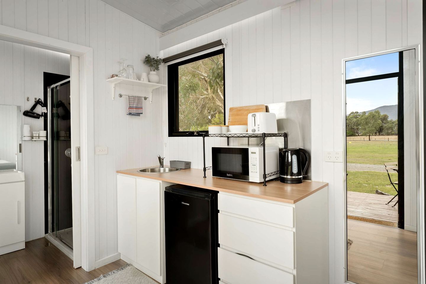 A modern kitchen with white cabinetry, a microwave, a coffee maker, and a window with a view of greenery.