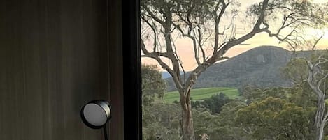 A bedroom with a bed, a bedside lamp, and a view of a rural landscape with trees and hills.