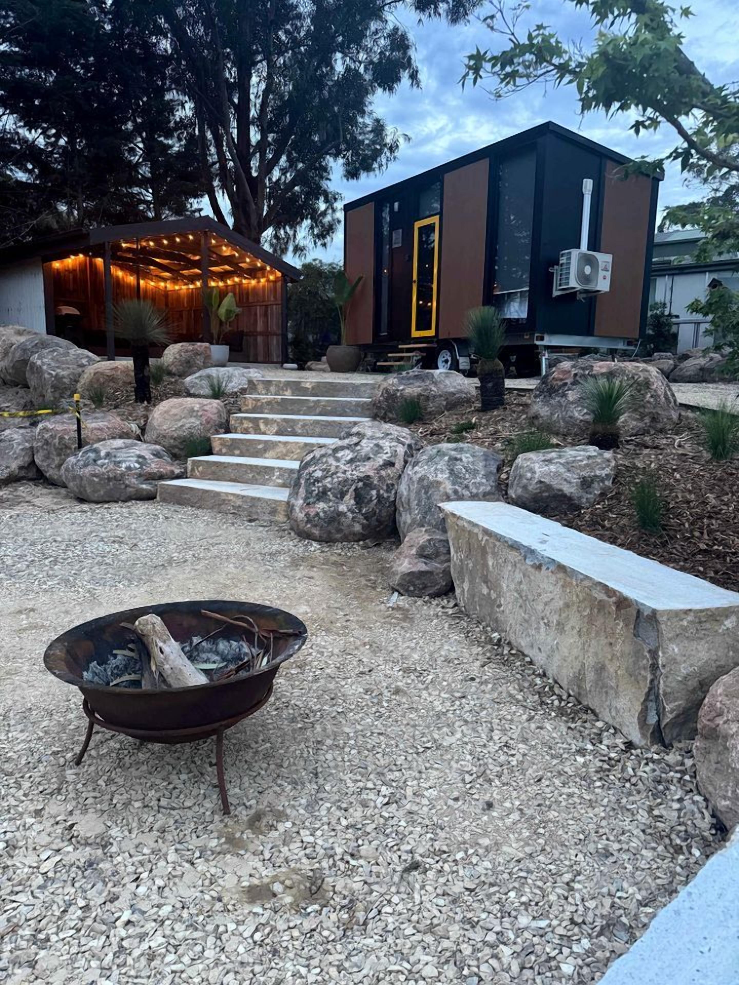 A modern outdoor area with a fire pit, stone steps, and a building with a yellow door.