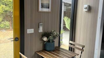 A compact room with a wooden table and two chairs, a potted plant, and a framed picture on the wall.