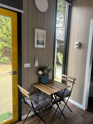 A compact room with a wooden table and two chairs, a potted plant, and a framed picture on the wall.