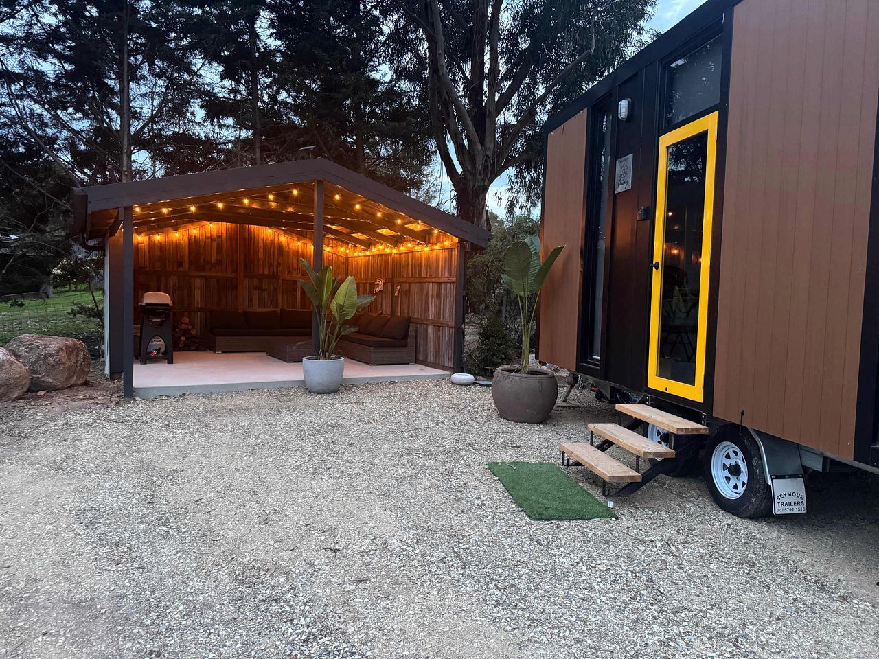 A wooden cabin with a covered porch and a yellow door, surrounded by trees and gravel.