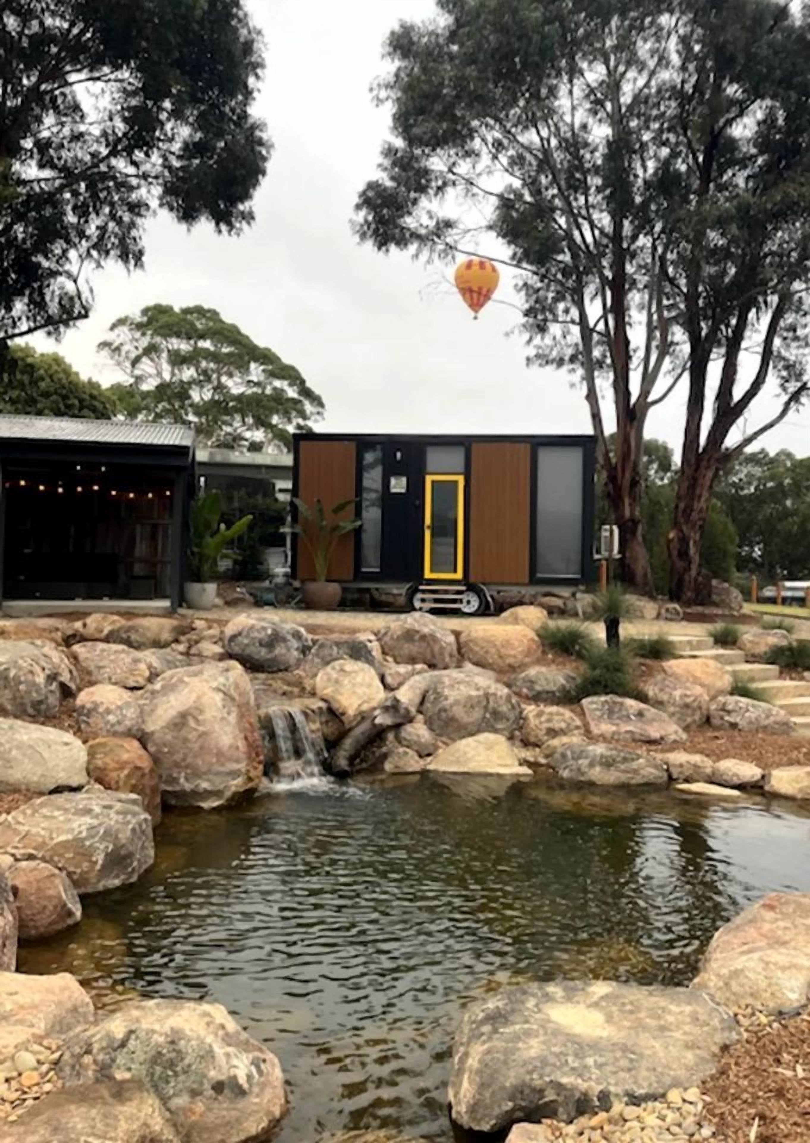 A modern building with a yellow door, surrounded by large rocks and a small waterfall.