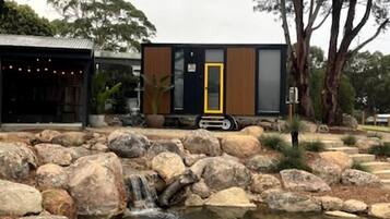 A modern building with a yellow door, surrounded by large rocks and a small waterfall.