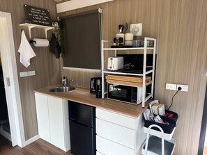 A compact kitchenette with a sink, a microwave, a coffee maker, and a small shelf with various items.