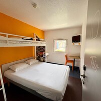 Una habitación de hotel con literas, un escritorio con silla, televisión y ventana con vistas.