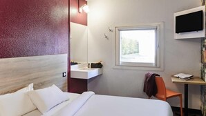 Quarto de hotel com cama, escrivaninha, cadeira, televisão e janela.