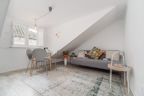 Une chambre de style loft moderne avec un plafond en pente, un coin repas avec des chaises, un canapé agrémenté de coussins décoratifs, une petite table d’appoint et un lampadaire.