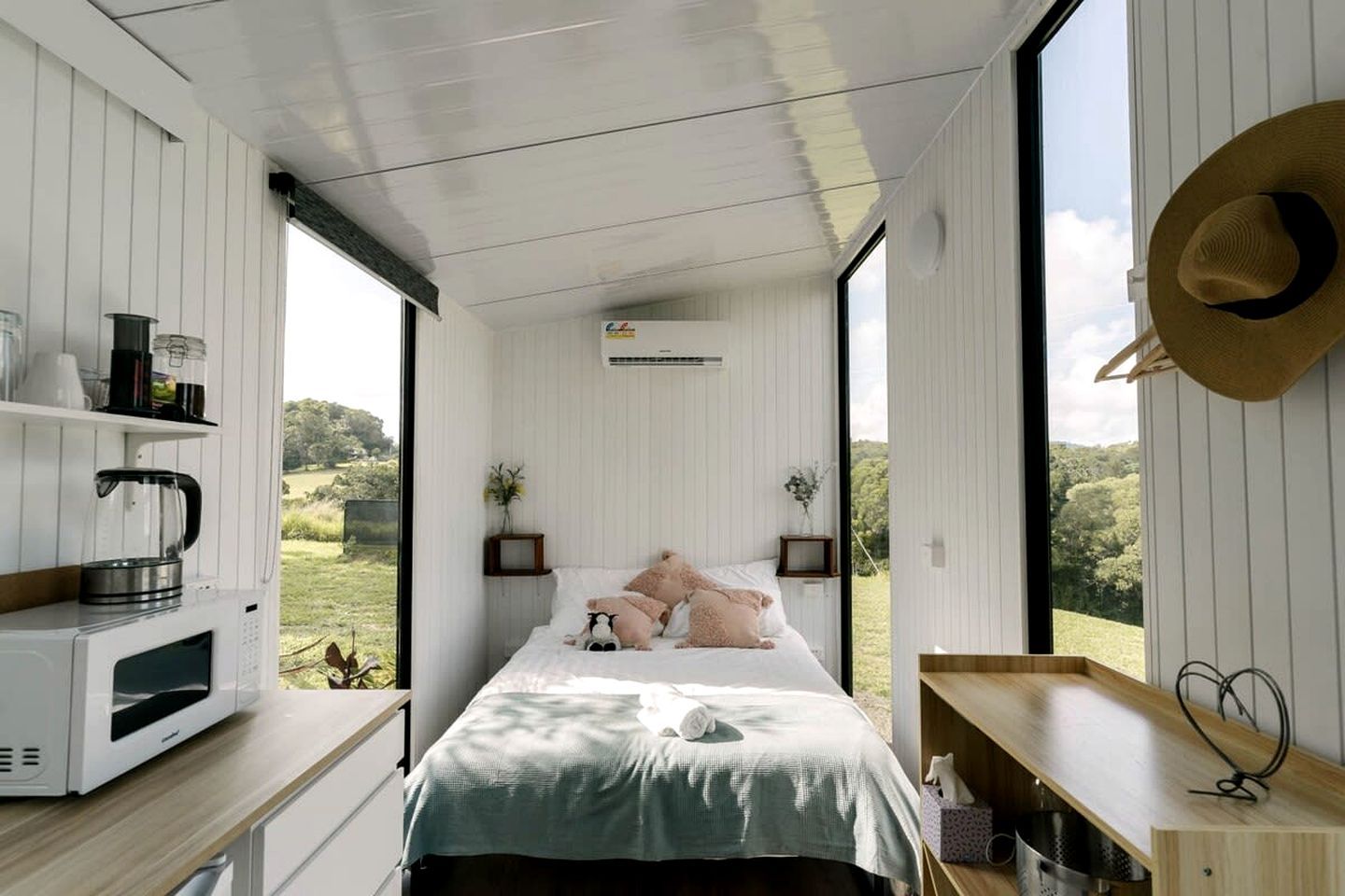 Un dormitorio con cama, mesitas de noche, vistas al exterior y una kitchenette.