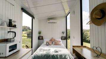 Un dormitorio con cama, mesitas de noche, vistas al exterior y una kitchenette.