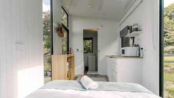 Un dormitorio pequeño con cama, estante de madera y kitchenette equipada con microondas.