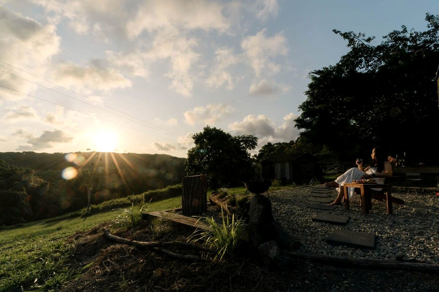 Atardecer sobre un paisaje rural con un banco de madera y una mesa donde dos personas están sentadas.