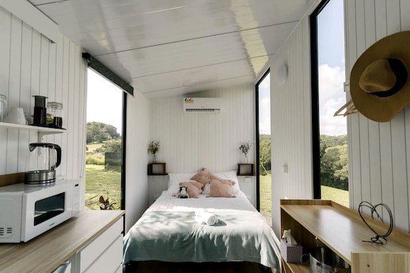 Un dormitorio con cama, mesitas de noche, vistas al exterior y una kitchenette.