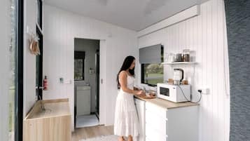 A compact kitchen with white cabinetry, a microwave, and a person preparing food.
