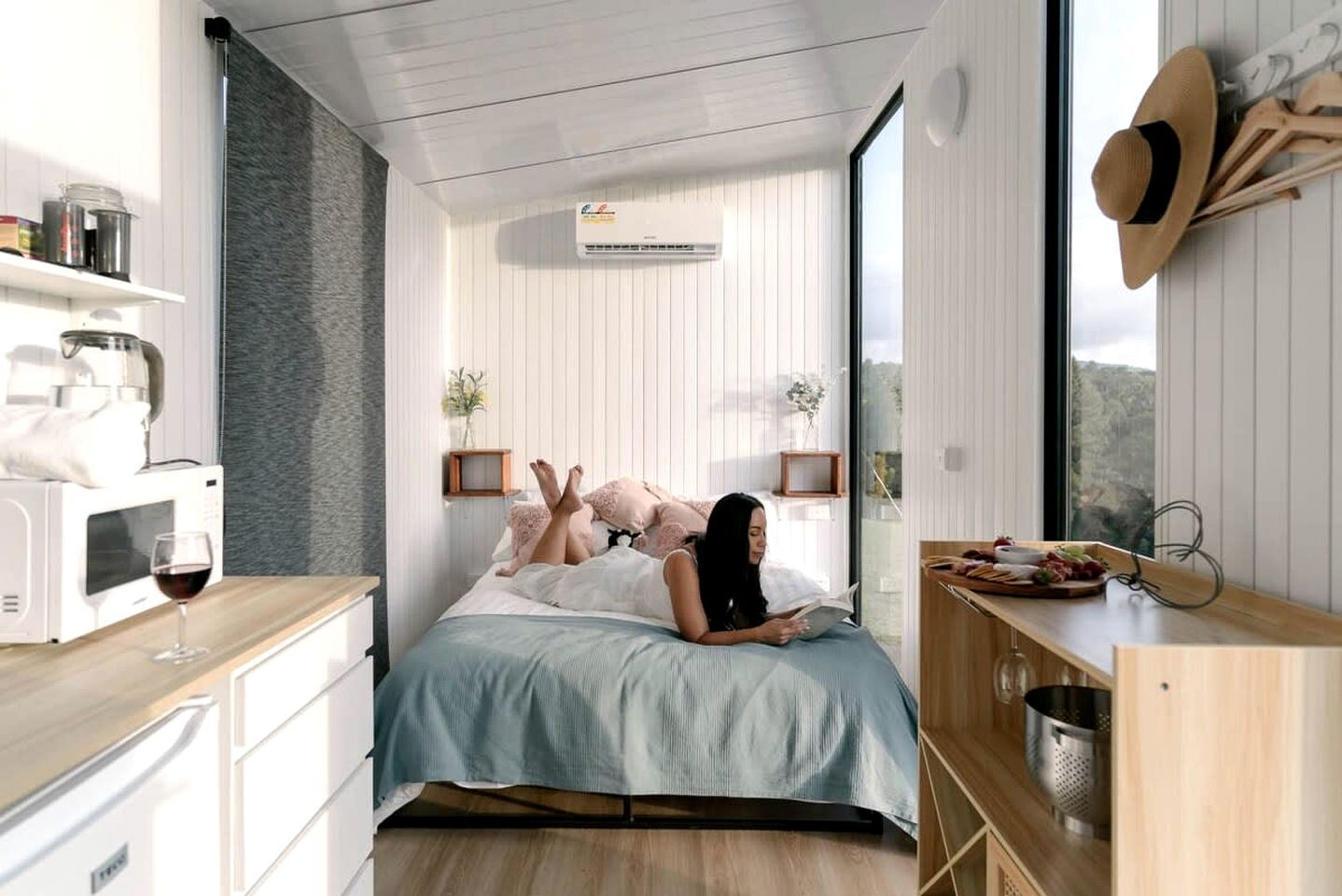 Een moderne slaapkamer met een bed, nachtkastjes, een magnetron, een wijnglas en uitzicht op het landschap.