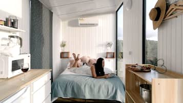 Een moderne slaapkamer met een bed, nachtkastjes, een magnetron, een wijnglas en uitzicht op het landschap.