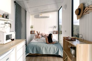 A modern bedroom with a bed, bedside tables, a microwave, a wine glass, and a view of the outdoors.